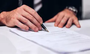 Dłoń mężczyzny w garniturze trzymająca pióro nad dokumentem.