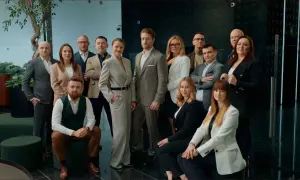 Grupa profesjonalistów w eleganckich strojach pozuje do zdjęcia w nowoczesnym wnętrzu.
