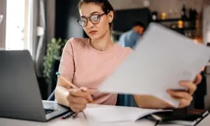 Kobieta w okularach pracuje przy biurku z laptopem i dokumentami.