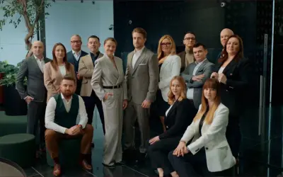 Grupa profesjonalistów w eleganckich strojach pozuje do zdjęcia w nowoczesnym wnętrzu.