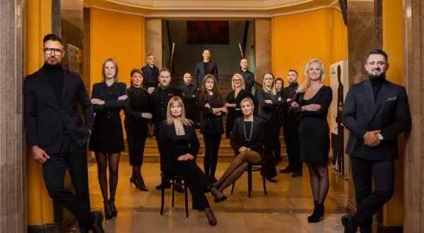 Grupa profesjonalistów w czarnych strojach pozuje w eleganckim wnętrzu.
