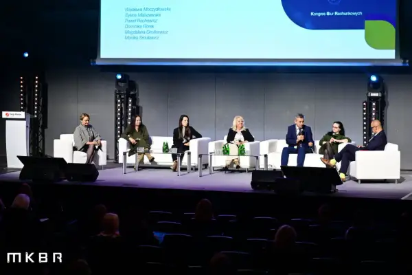 Panel dyskusyjny z udziałem ekspertów na scenie, siedzących na białych sofach.